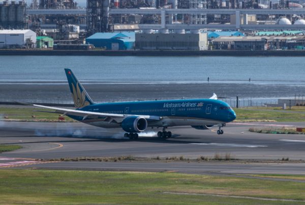 a blue and white jet airliner on runway next to water